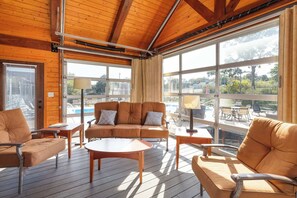 Une terrasse en bois avec un canapé, des chaises et une table, donnant sur une piscine et un espace de détente extérieur.