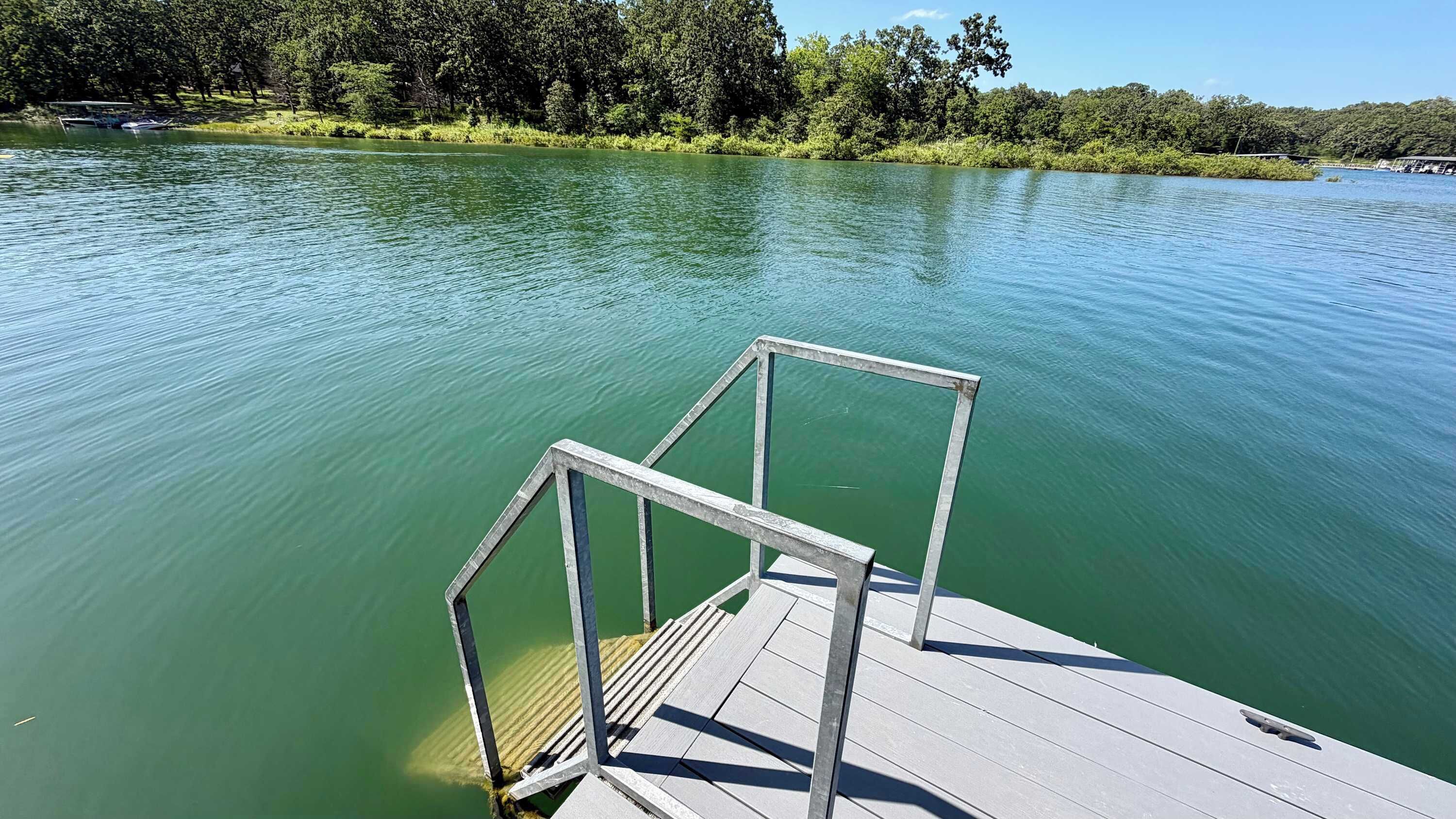 Une jetée en bois s’étendant dans un lac paisible, avec une rambarde en métal, et entourée d’une végétation luxuriante.