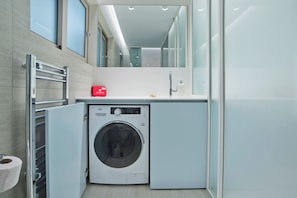 A compact, modern bathroom with a built-in washing machine, a first aid kit, and a towel rack.