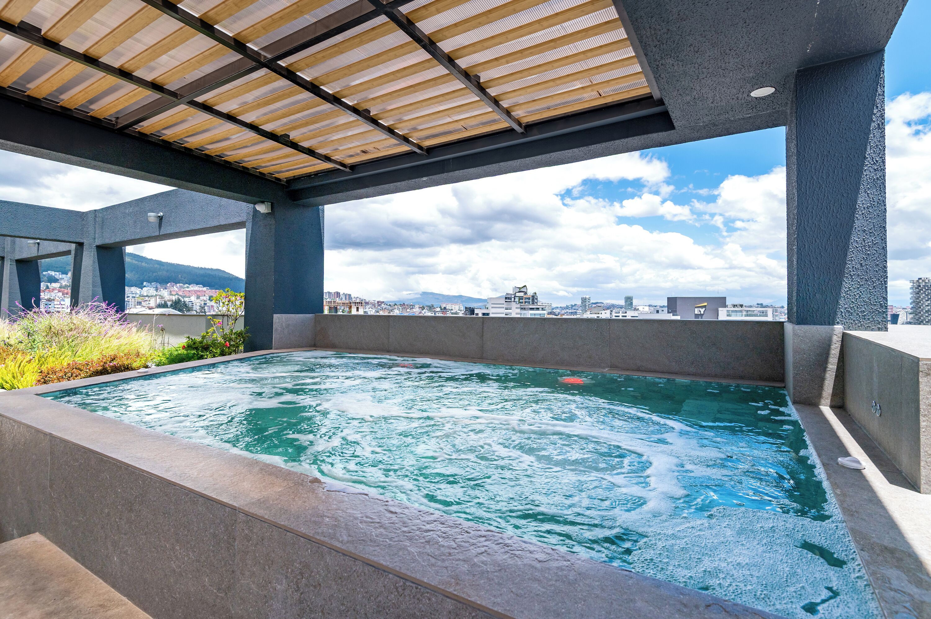 A rooftop hot tub with a city view, surrounded by modern architecture and a wooden pergola.