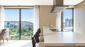 A modern kitchen with a large island, a dining area with chairs, and large windows offering a city view. - Edificio Efyra by Host Ecuador (Quito)