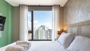 A hotel room with a large bed, a view of the cityscape, and a flat-screen TV mounted on the wall. - Edificio Efyra by Host Ecuador (Quito)