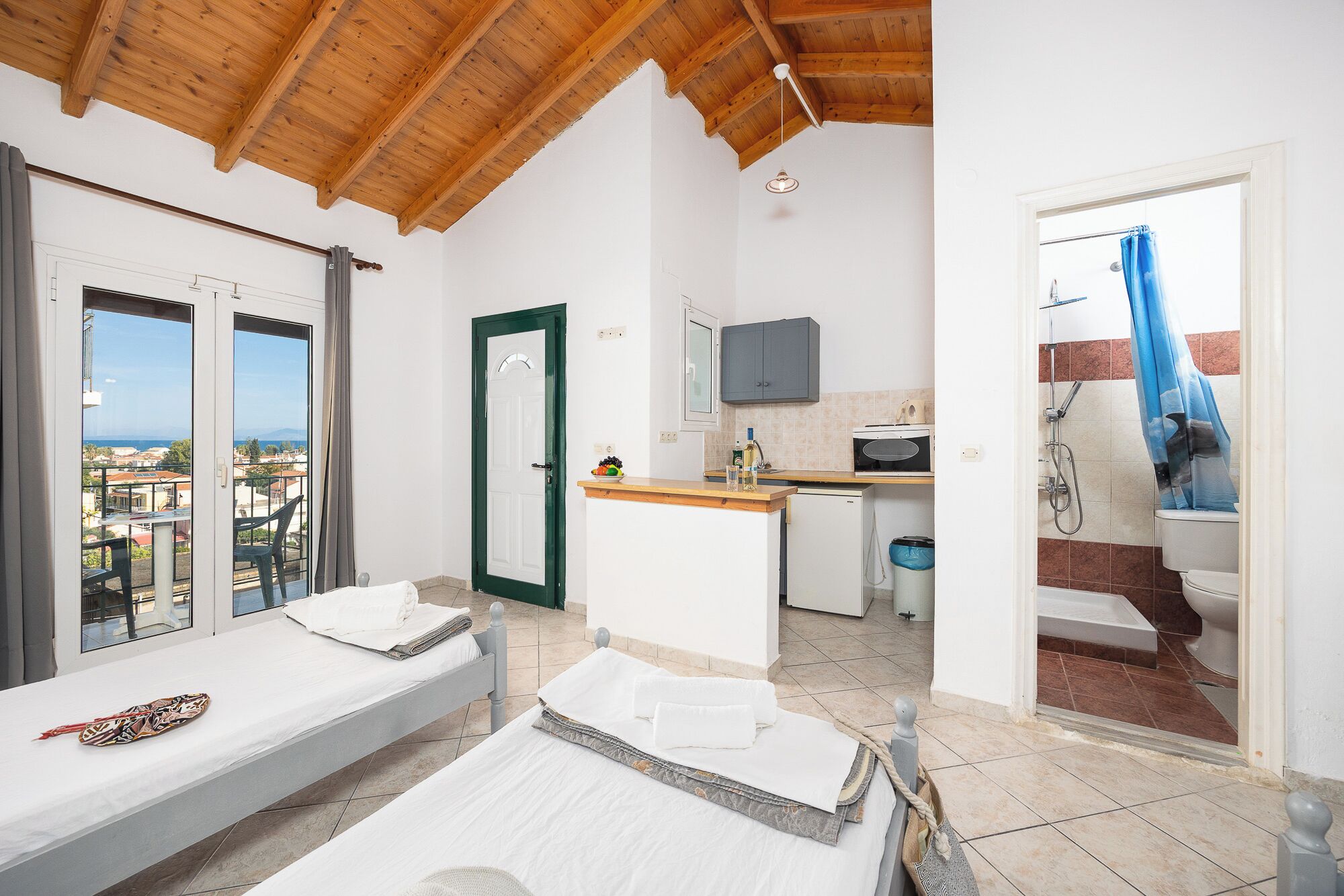 Habitación de hotel con balcón, kitchenette, ducha y cama con toallas.