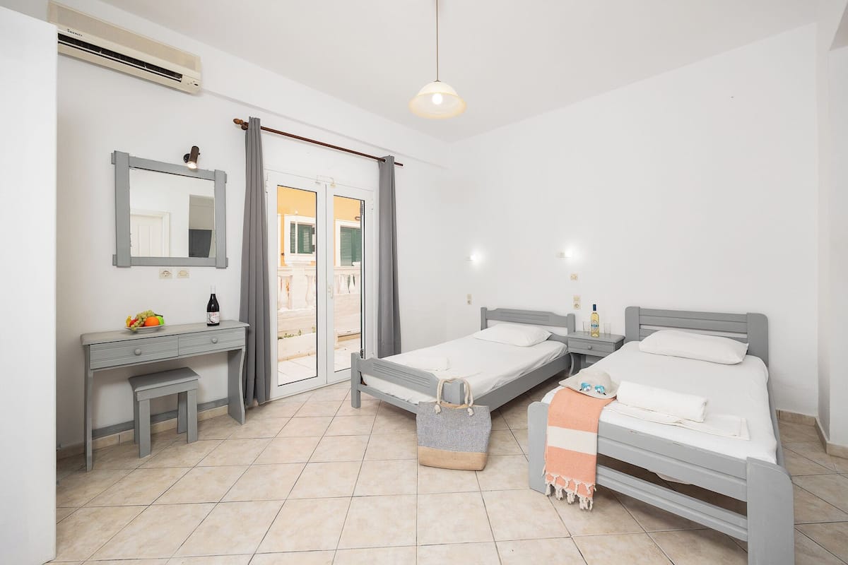 Une chambre à coucher avec deux lits simples, une table de chevet avec une bouteille, un miroir et une fenêtre avec des rideaux.
