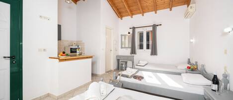 A small, clean room with a wooden ceiling, a bed, a bedside table, a mirror, and a small kitchenette.