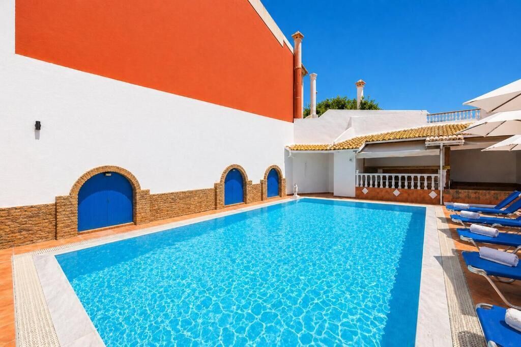 A swimming pool with blue tiles, a white wall with a red section, and blue doors.