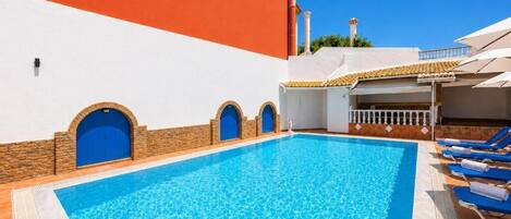 A swimming pool with blue tiles, a white wall with a red section, and blue doors.