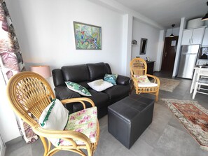 A living room with a black sofa, two wicker chairs, a black ottoman, and a colorful painting on the wall.