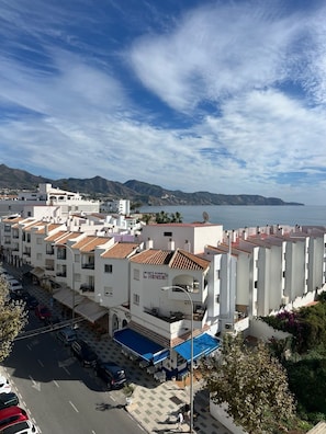 A residential building with multiple balconies, a blue awning, and a view of the sea.