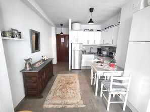 A compact kitchen with white cabinets, a stainless steel refrigerator, a dining table with chairs, and a rug on the floor.