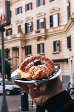 A hand holding a plate with a croissant.