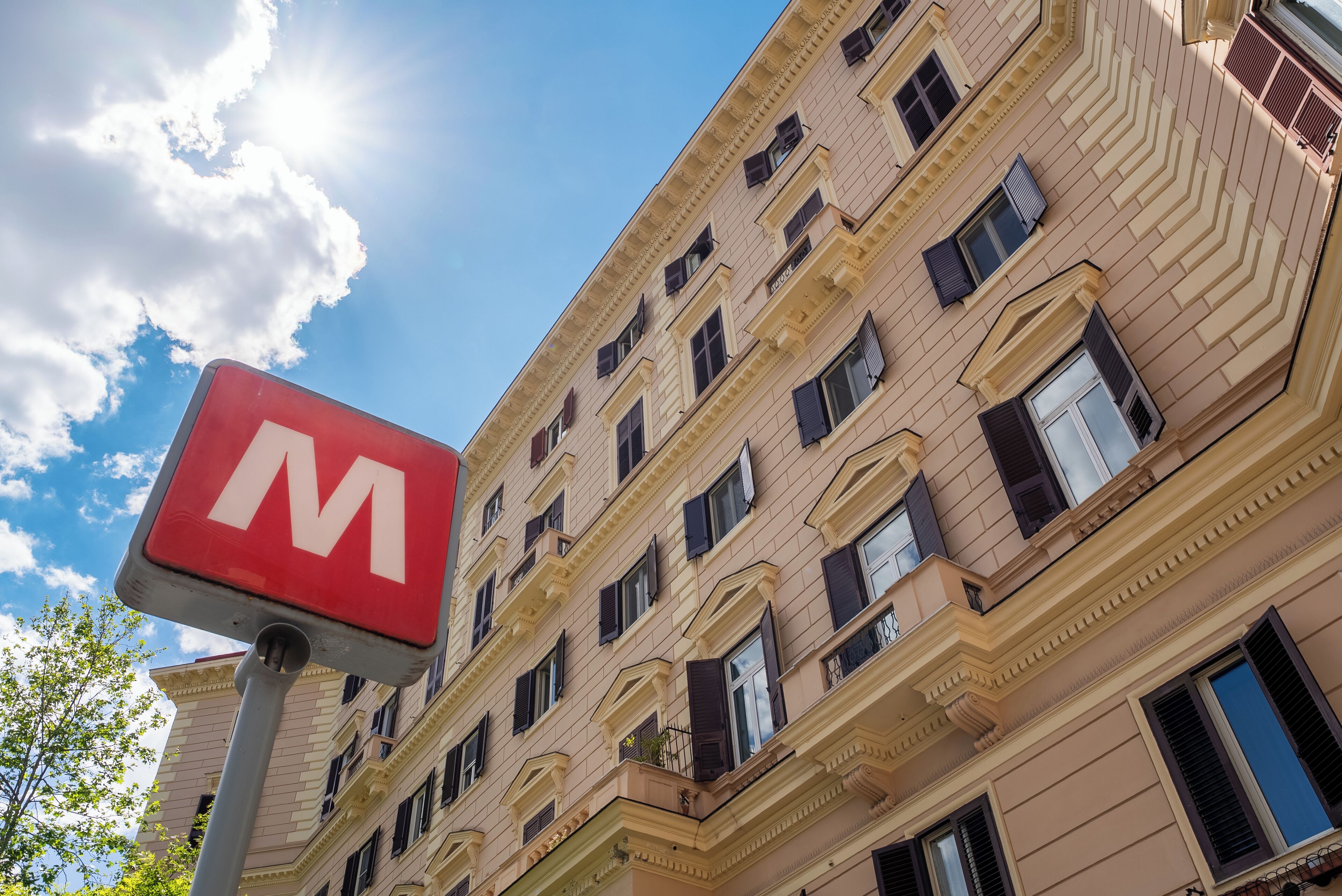 Un edificio con un llamativo letrero rojo en forma de 'M', varias ventanas y un cielo despejado.