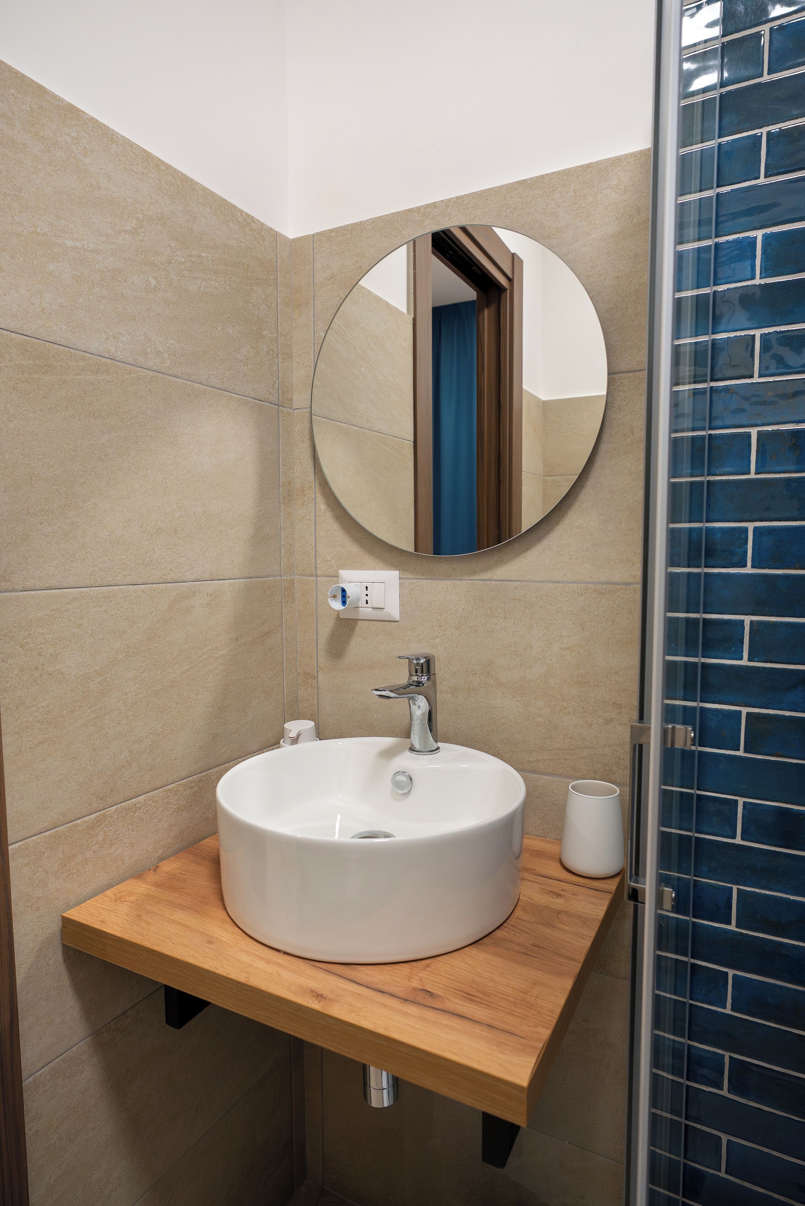 A bathroom with a round mirror, a white sink, and a wooden countertop.