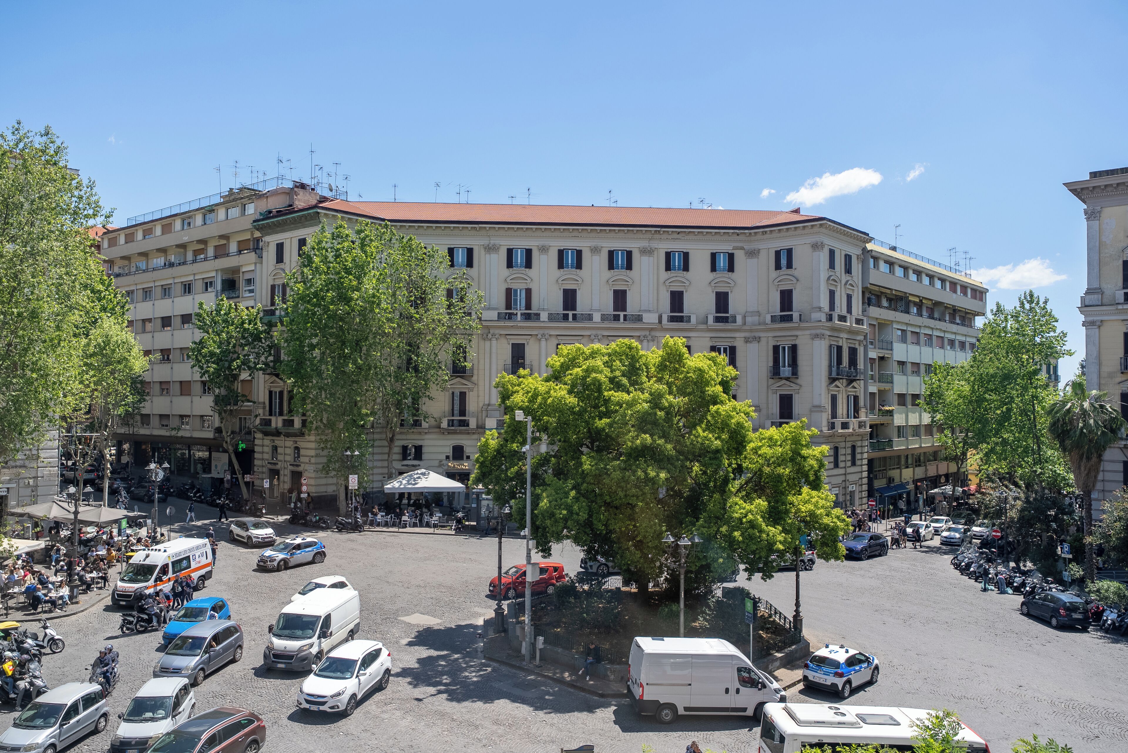 A multi-story building with a central courtyard, surrounded by parked cars and trees.