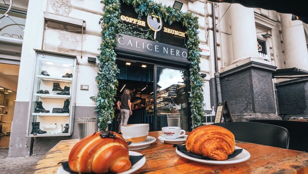 A wooden table with croissants and coffee cups in front of a coffee shop named Calice Nero. - l'abbraccio di Maria (Naples)