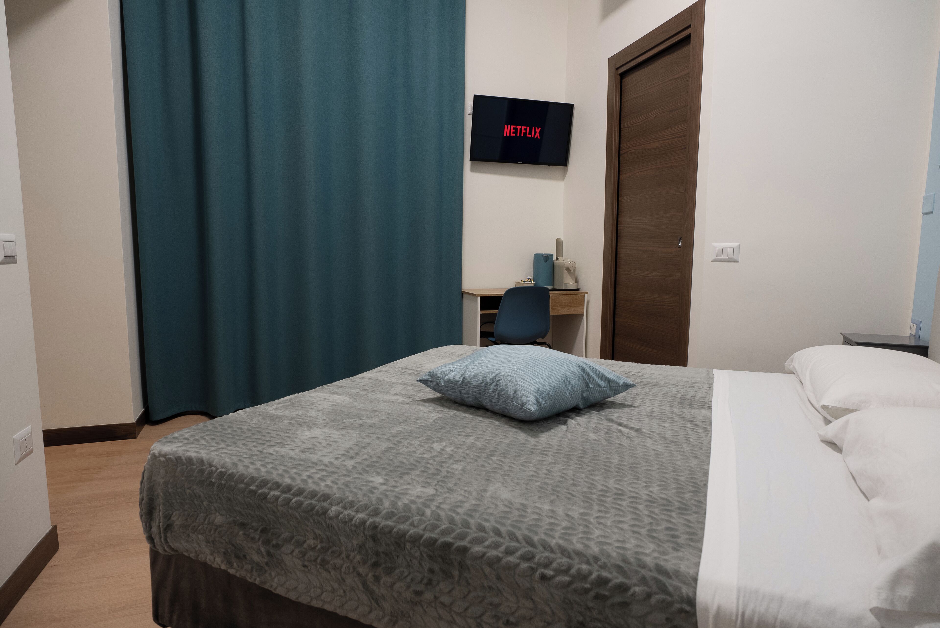 A hotel room with a bed, a desk, a chair, a TV mounted on the wall, and a door.
