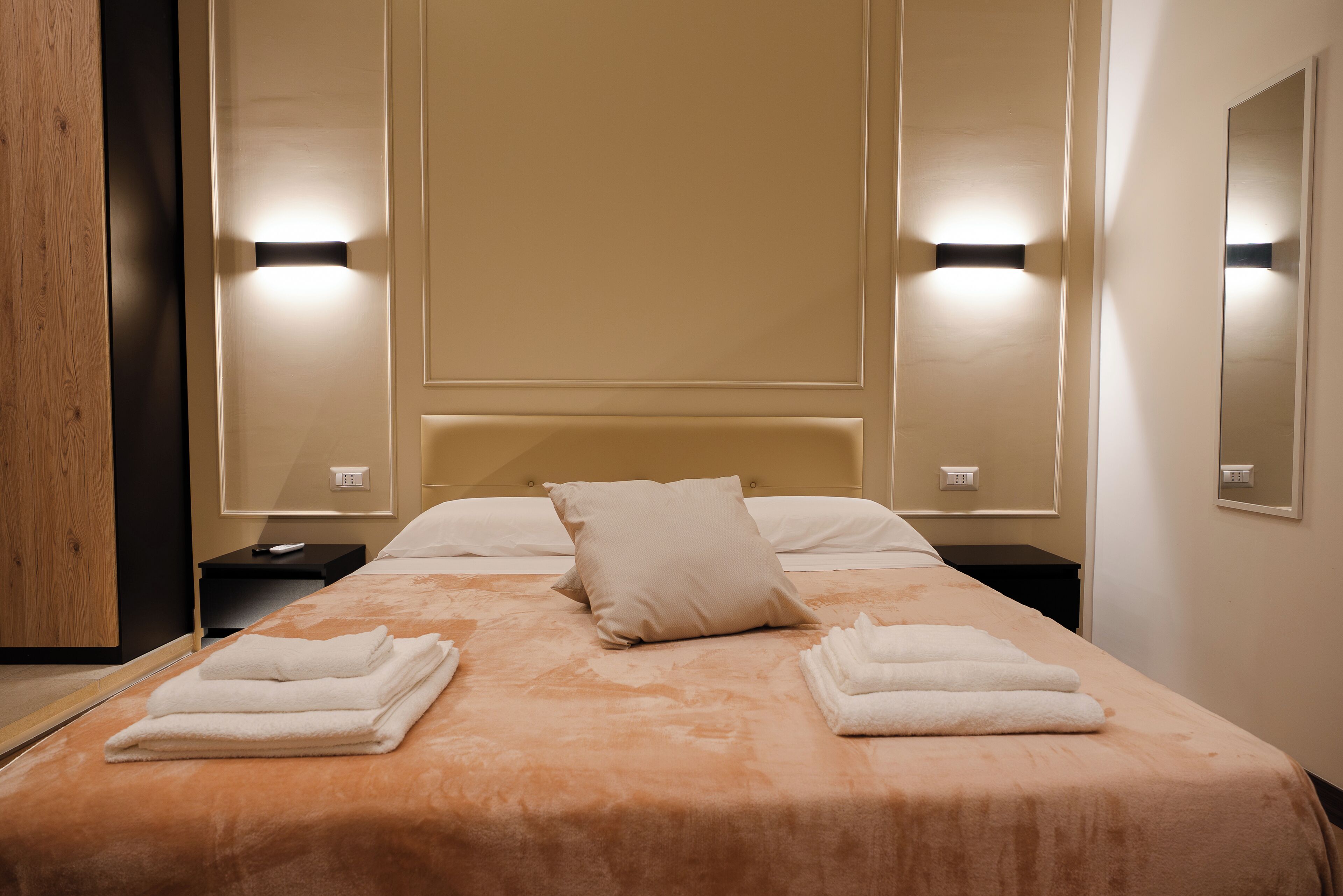 Ein Hotelzimmer mit einem großen Bett, zwei Nachttischen, einem Spiegel und Wandleuchten.
