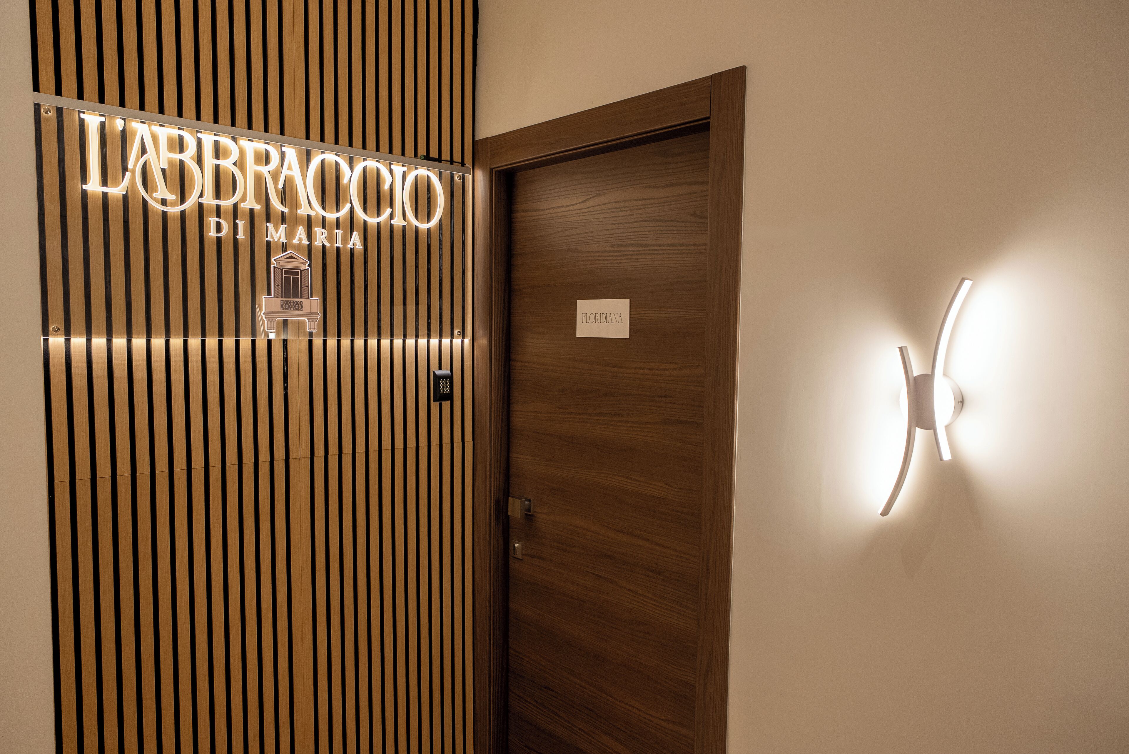 A hotel entrance with a sign reading "LABBRACCI DI MARIA" and a wooden door with a nameplate.