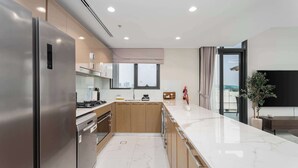 Una cocina moderna con un refrigerador de acero inoxidable, armarios de madera, encimera de mármol y vistas a la ciudad a través de amplios ventanales.