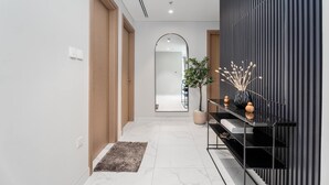Un pasillo moderno con piso de mármol, una puerta de madera, un espejo, una consola negra con objetos decorativos y una pared a rayas.