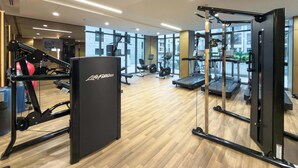 Un gimnasio con máquinas de cardio, equipo de pesas y un espejo grande.