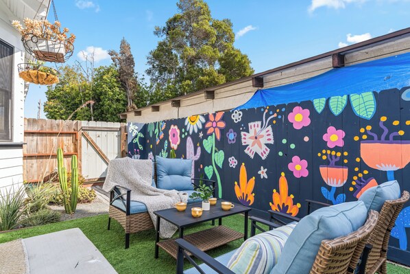 Un patio con muebles de exterior, una mesa con tazas y una pared decorada con coloridas ilustraciones florales.