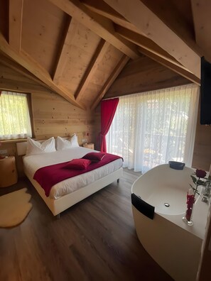 A wooden cabin bedroom with a large bed, a bathtub, and a window with curtains.