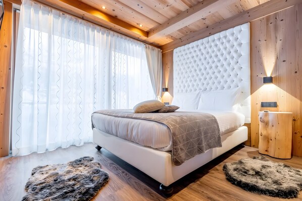 A bedroom with a large bed, wooden ceiling beams, a wall-mounted light, and a rug.