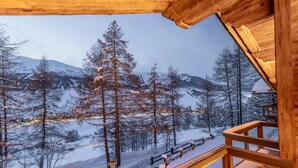 Una cabaña de madera con balcón que da a un paisaje montañoso nevado.