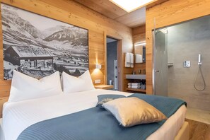 A wooden-paneled room with a bed, a wall-mounted lamp, a bathroom with a shower, and a large black-and-white photo.