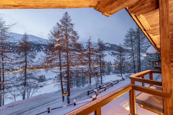 A wooden cabin with a balcony overlooking a snowy mountain landscape.