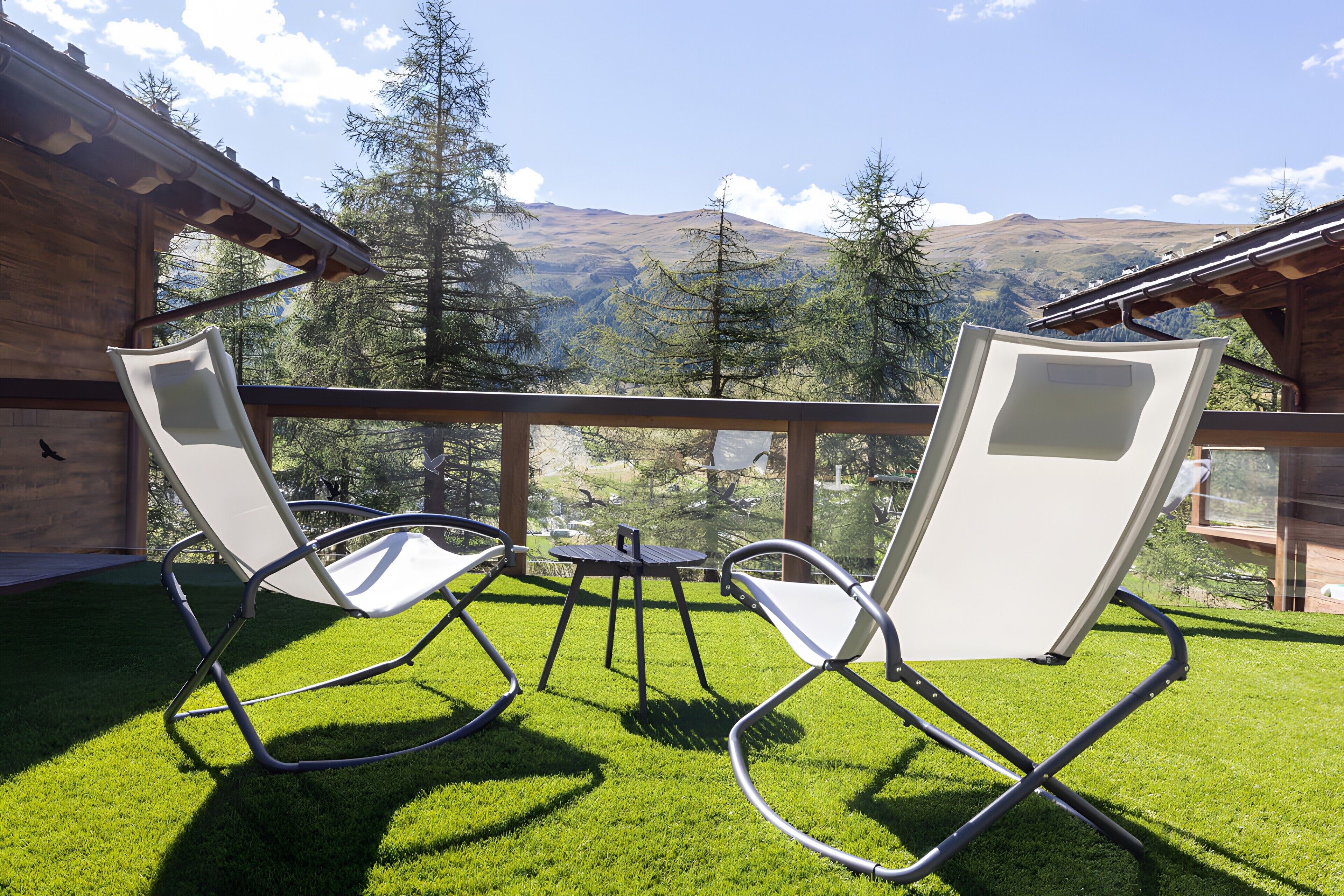 Un balcón con dos sillas blancas y una mesa pequeña, con vistas a un paisaje montañoso.