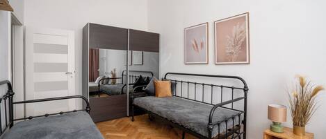 A compact bedroom with two single beds, a wardrobe, a mirror, and two framed wall art pieces.