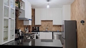 Een moderne keuken met witte kasten, een centraal kookeiland met barkrukken, een inbouwoven en een koelkast.