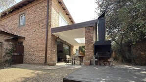 Een bakstenen huis met een terras, een barbecue en een overdekte zithoek.