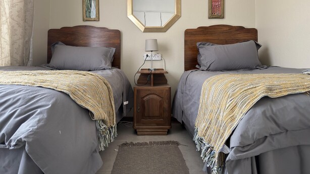 Een slaapkamer met twee bedden, een nachtkastje met lamp en een spiegel aan de muur.