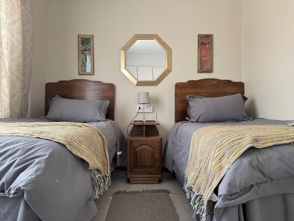 Un dormitorio con dos camas, una mesita de noche con una lámpara y un espejo en la pared.