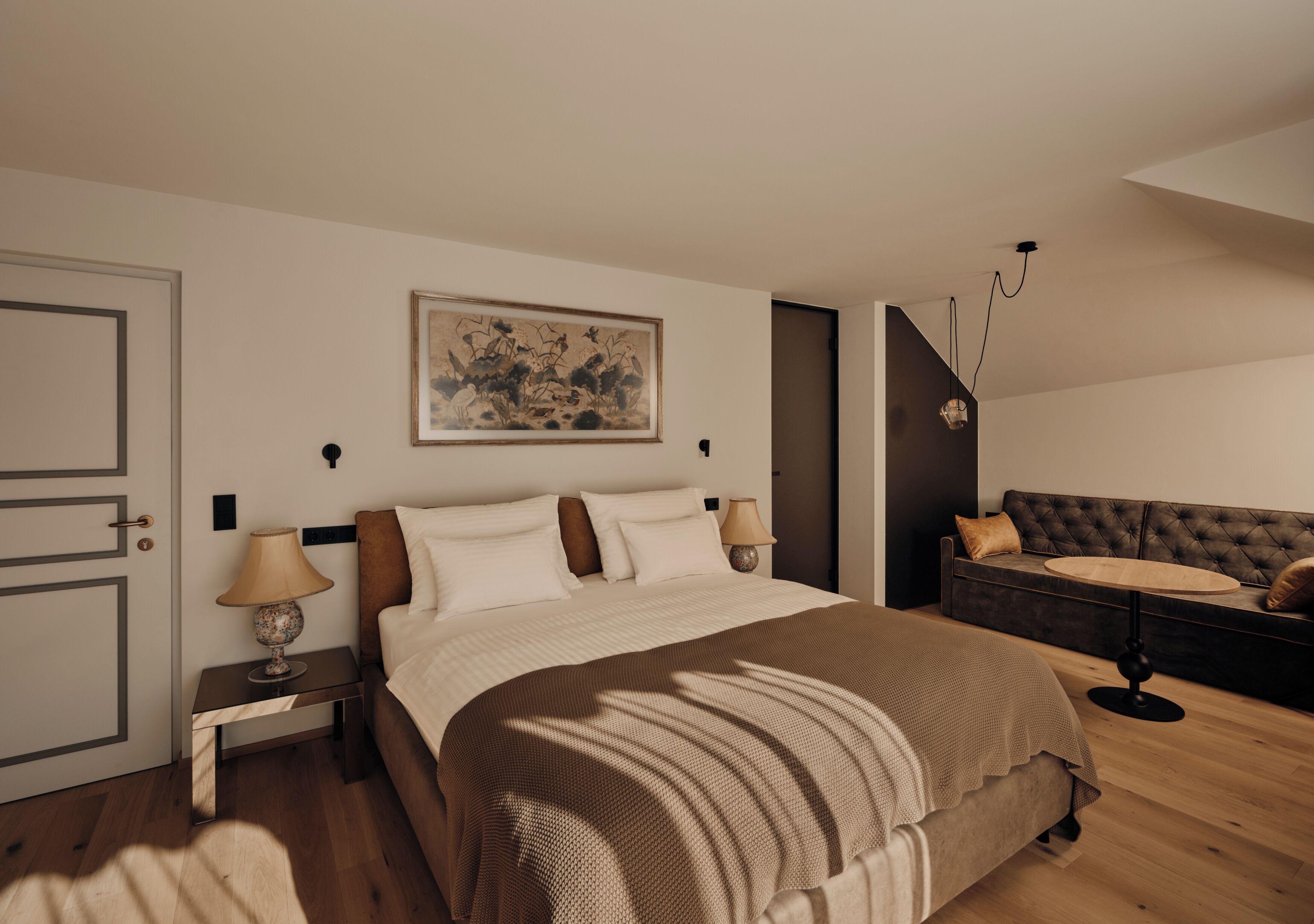 A bedroom with a bed, bedside tables, a lamp, a painting, a sofa, and a hanging light fixture.