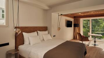 A bedroom with a large bed, a round side table, a chair, a TV, and a balcony with a table and chair.