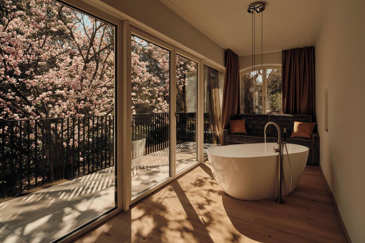 A modern bathroom with a freestanding bathtub, large windows, and a view of cherry blossoms.