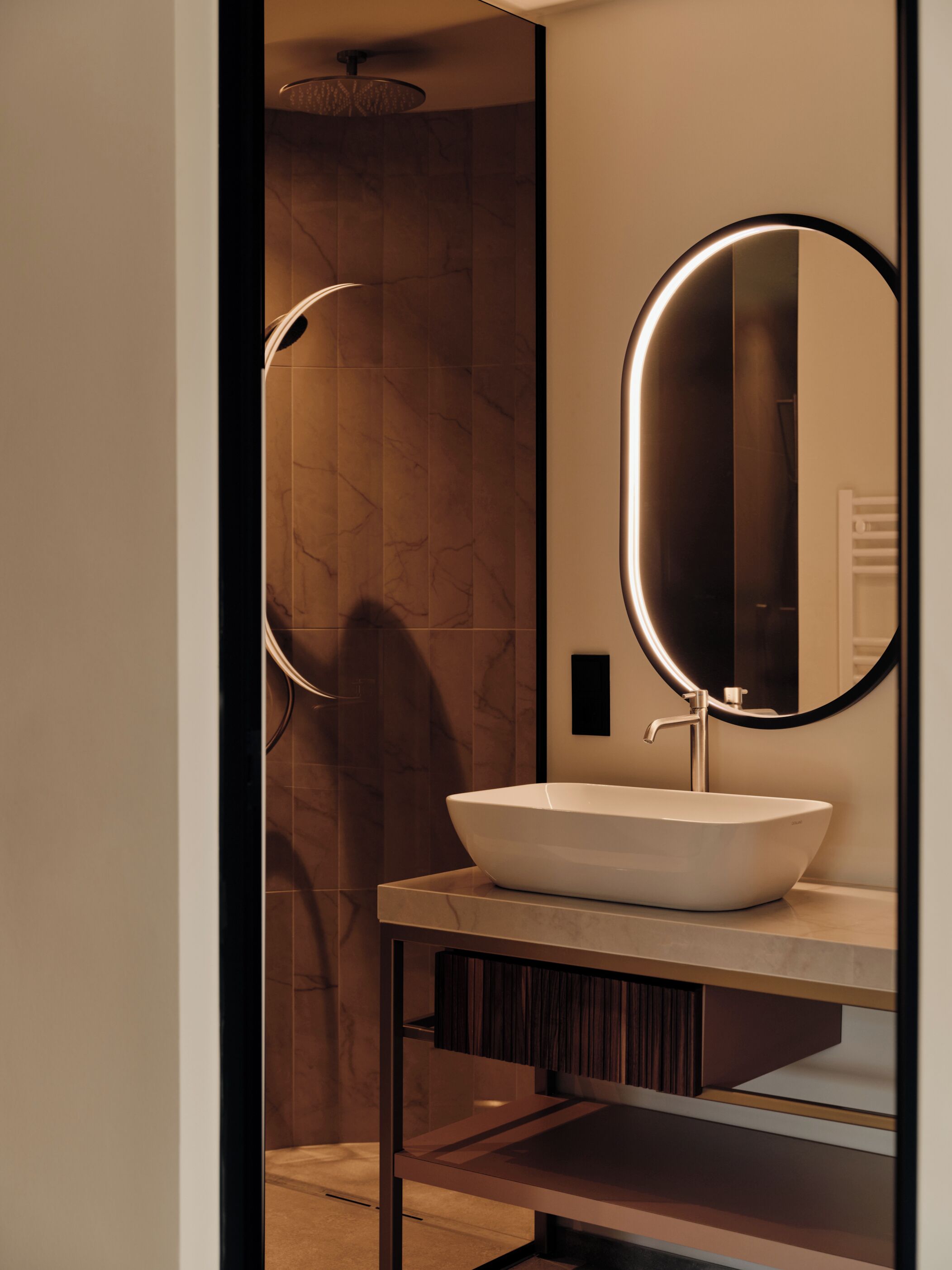 A modern bathroom with a large oval mirror, a white vessel sink, and a shower with a curved design.