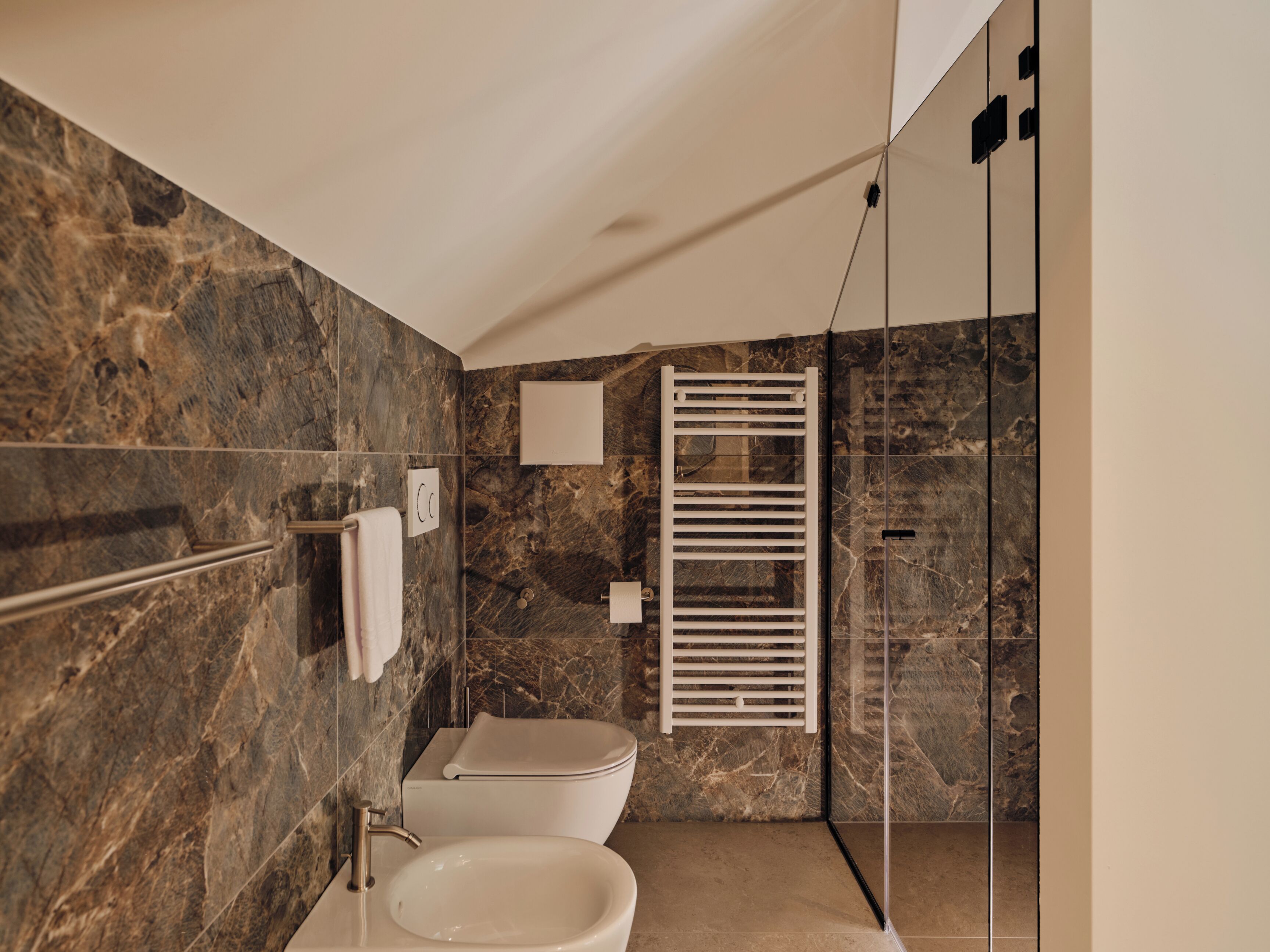 Ein modernes Badezimmer mit Marmorwand, Toilette, Waschbecken und einer Duschkabine aus Glas.