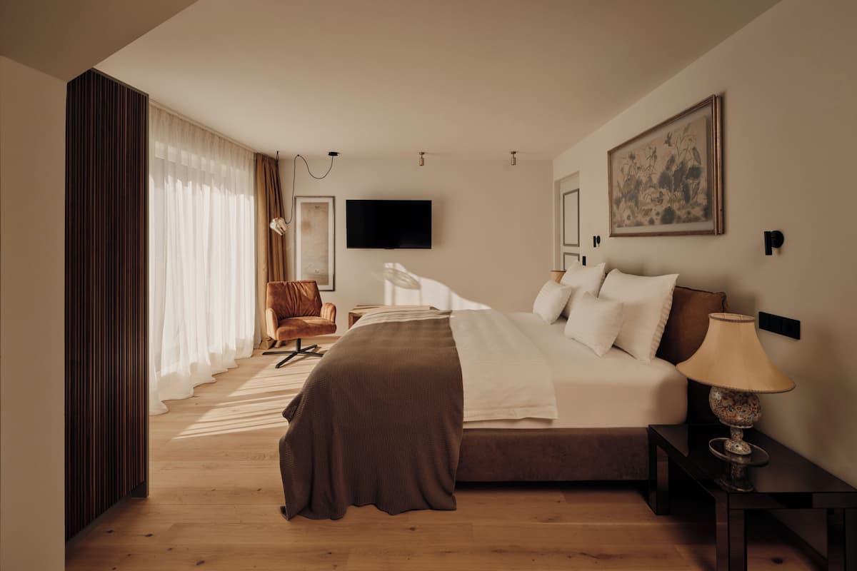 A modern hotel room with a large bed, a desk, a chair, and a TV.