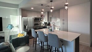 A modern kitchen with a central island, bar stools, stainless steel appliances, and pendant lighting.