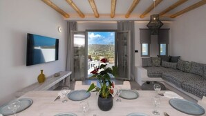 A modern living room with a dining area, a sofa, and a TV mounted on the wall.