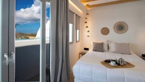 A hotel room with a large bed, a view through a sliding door, and a balcony with a clear sky.