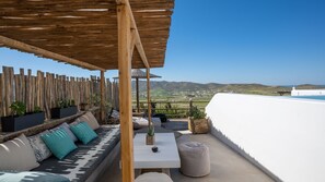 A rooftop terrace with a wooden pergola, a sofa with cushions, a table, and potted plants.