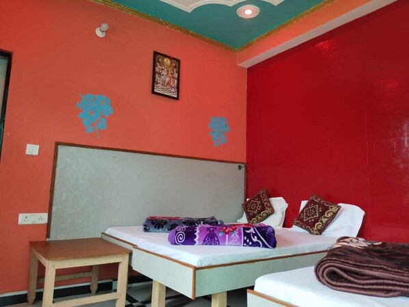 A room with two beds, a small table, and a ceiling with decorative molding. - Hotel Rudra (Rajgarhi)