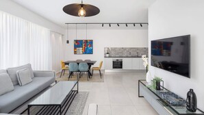 Una sala de estar moderna con sofá, mesa de centro, comedor, sillas y una zona de cocina con televisor.