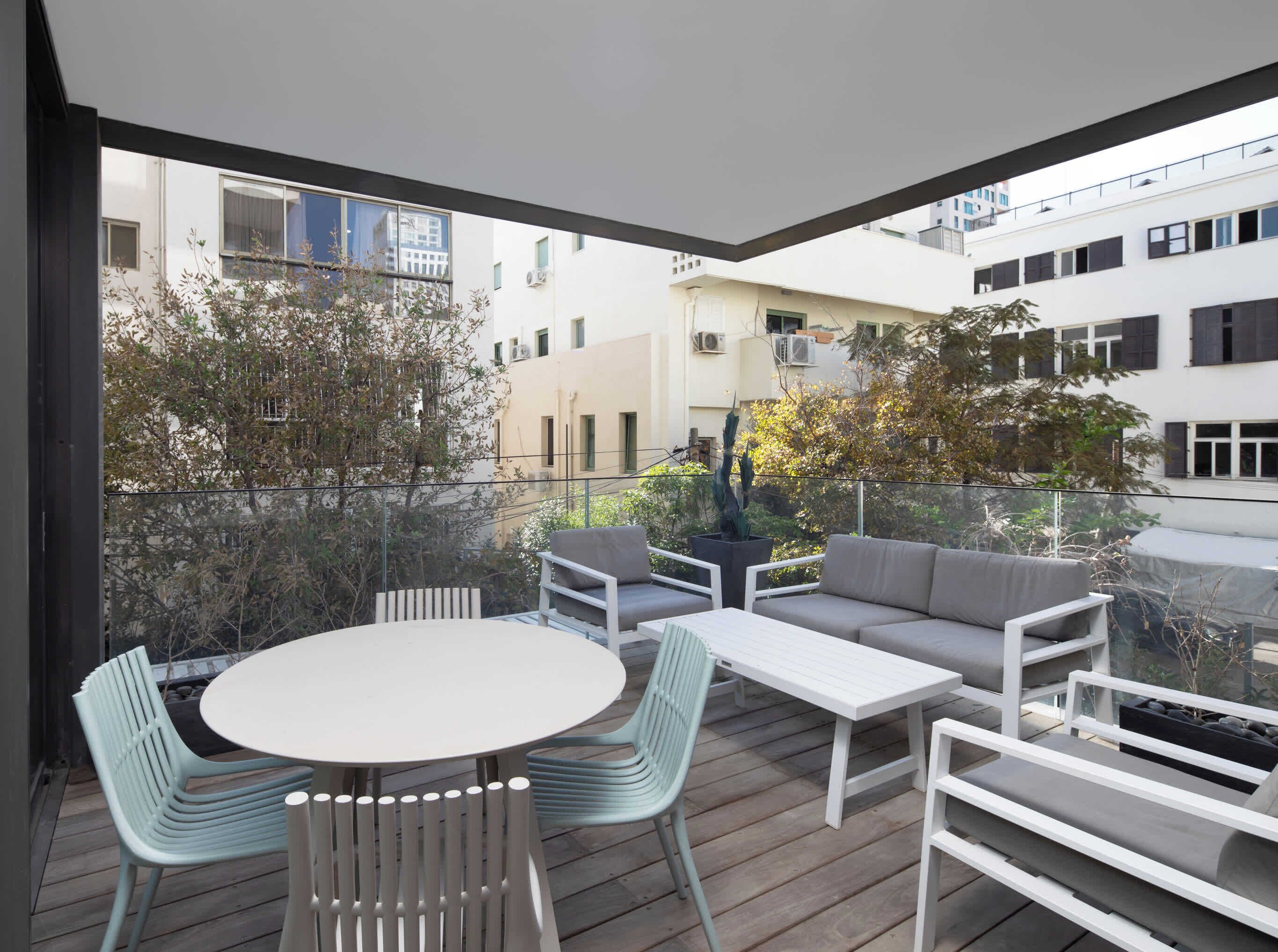 A modern outdoor patio with a round table and chairs, a sofa, and a white coffee table.